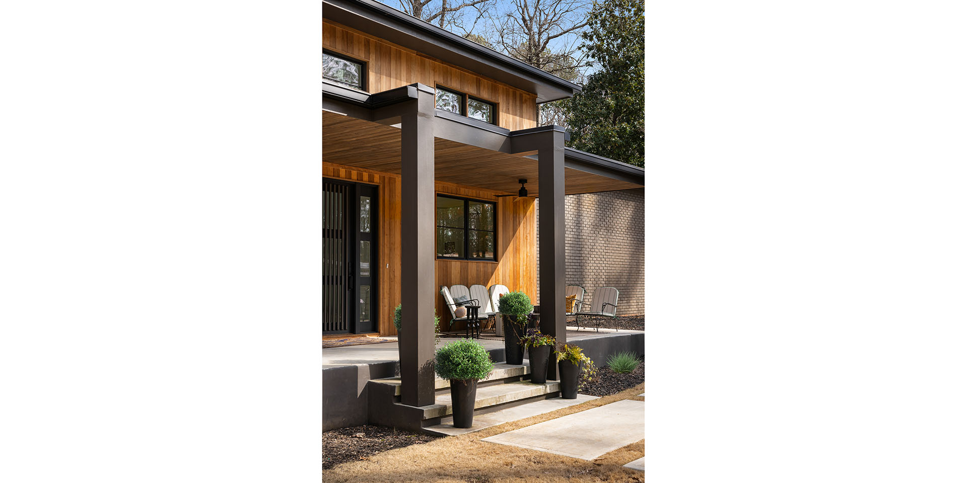 Modern wooden-clad porch of a contemporary home with dark posts, planters, and outdoor seating.