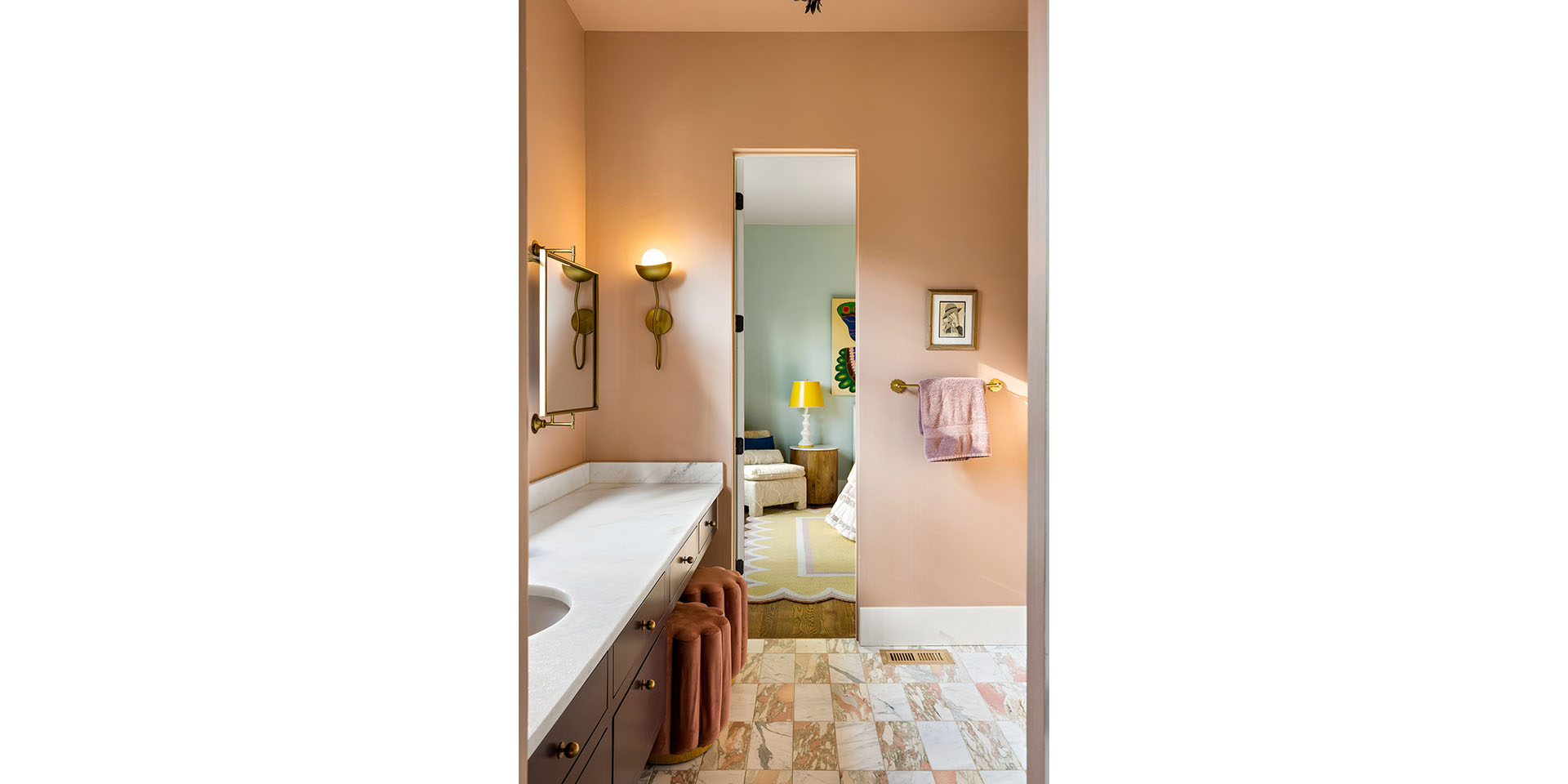 Bathroom vanity with marble countertop and peach walls, pink towels on the rack, leading to a pastel-colored bedroom.