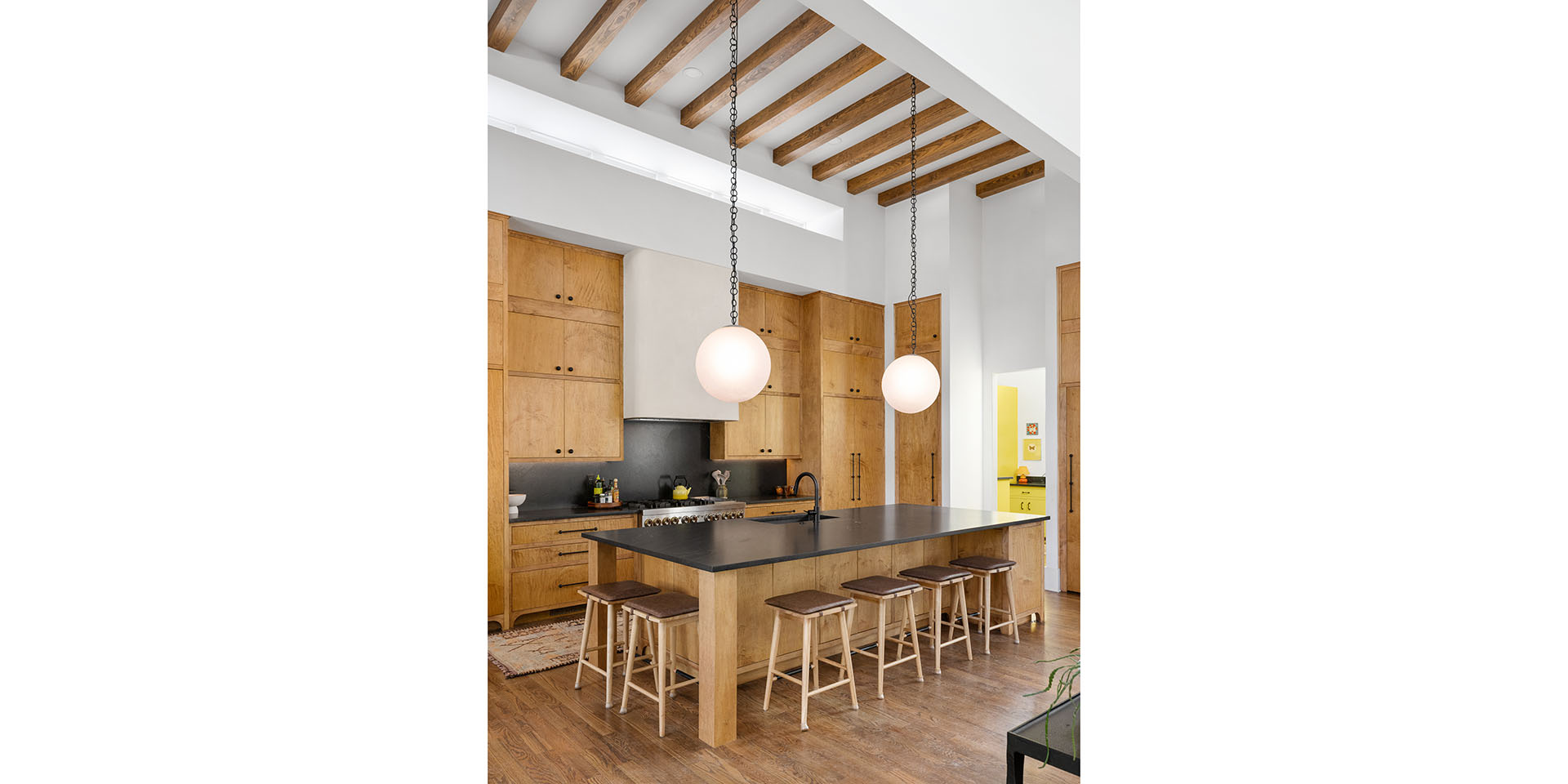 Open kitchen with a wooden island, stools, and two globe pendant lights under exposed ceiling beams.