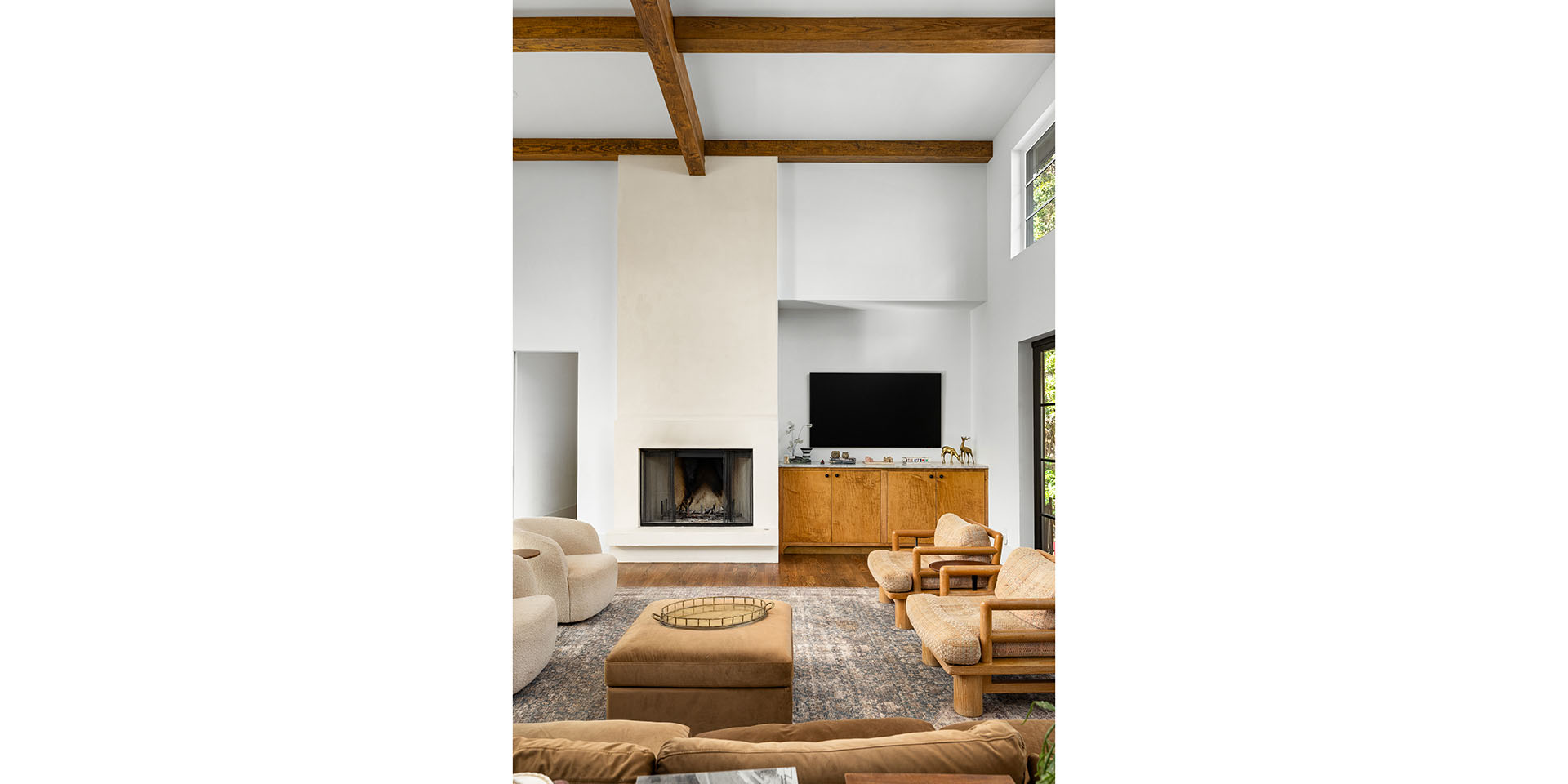Modern living room with a tall white fireplace, exposed wooden beams, and a TV above a wooden cabinet.