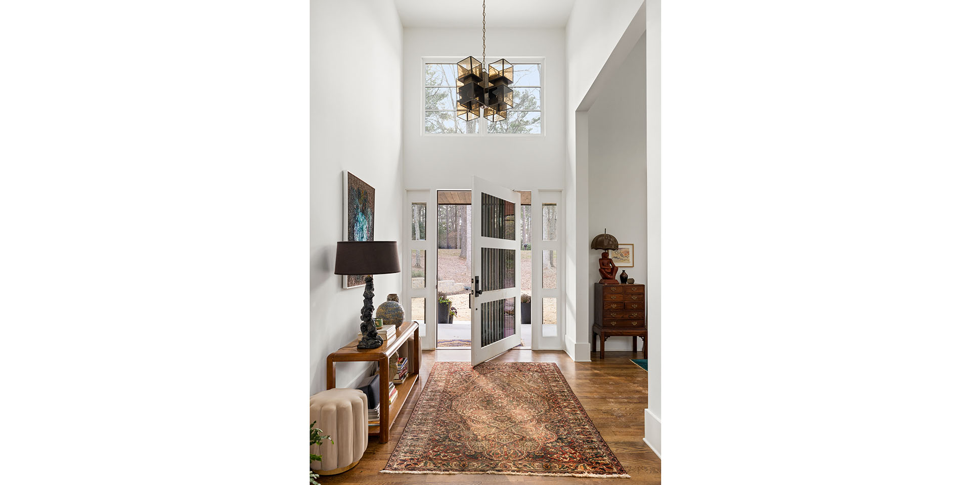 Bright entryway with open double doors to a yard, a patterned rug, and a tall chandelier overhead.