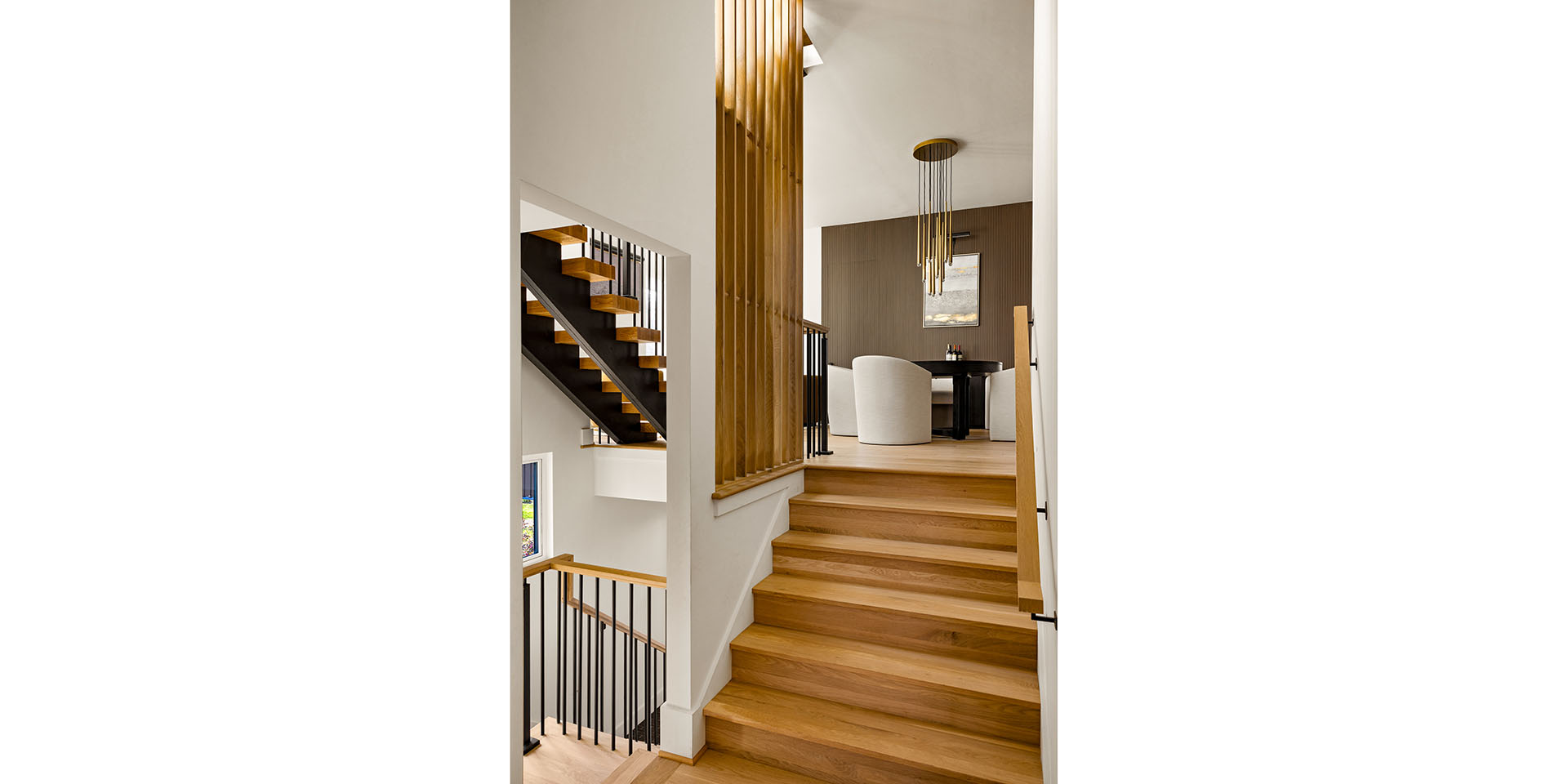 Modern multi-level interior with a wooden staircase, metal rails, and a seating area visible on the upper level.