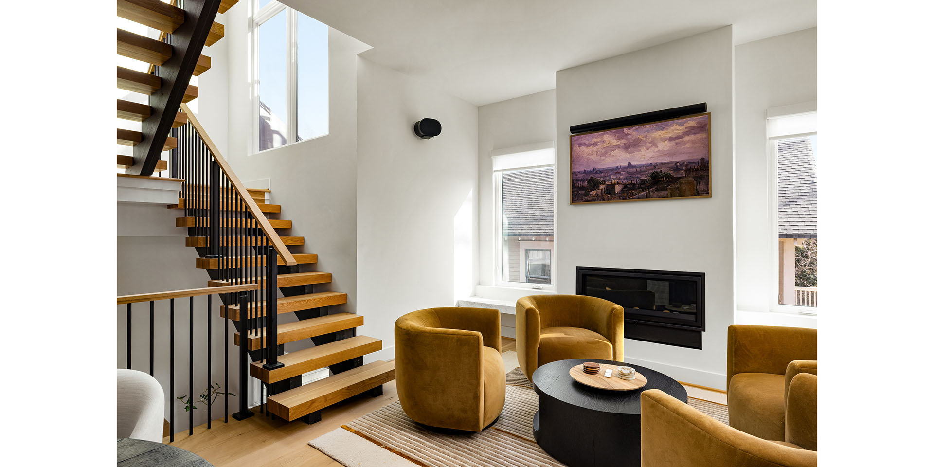 Modern living room with an open wooden staircase, white walls, a gas fireplace, and mustard armchairs around a round coffee table