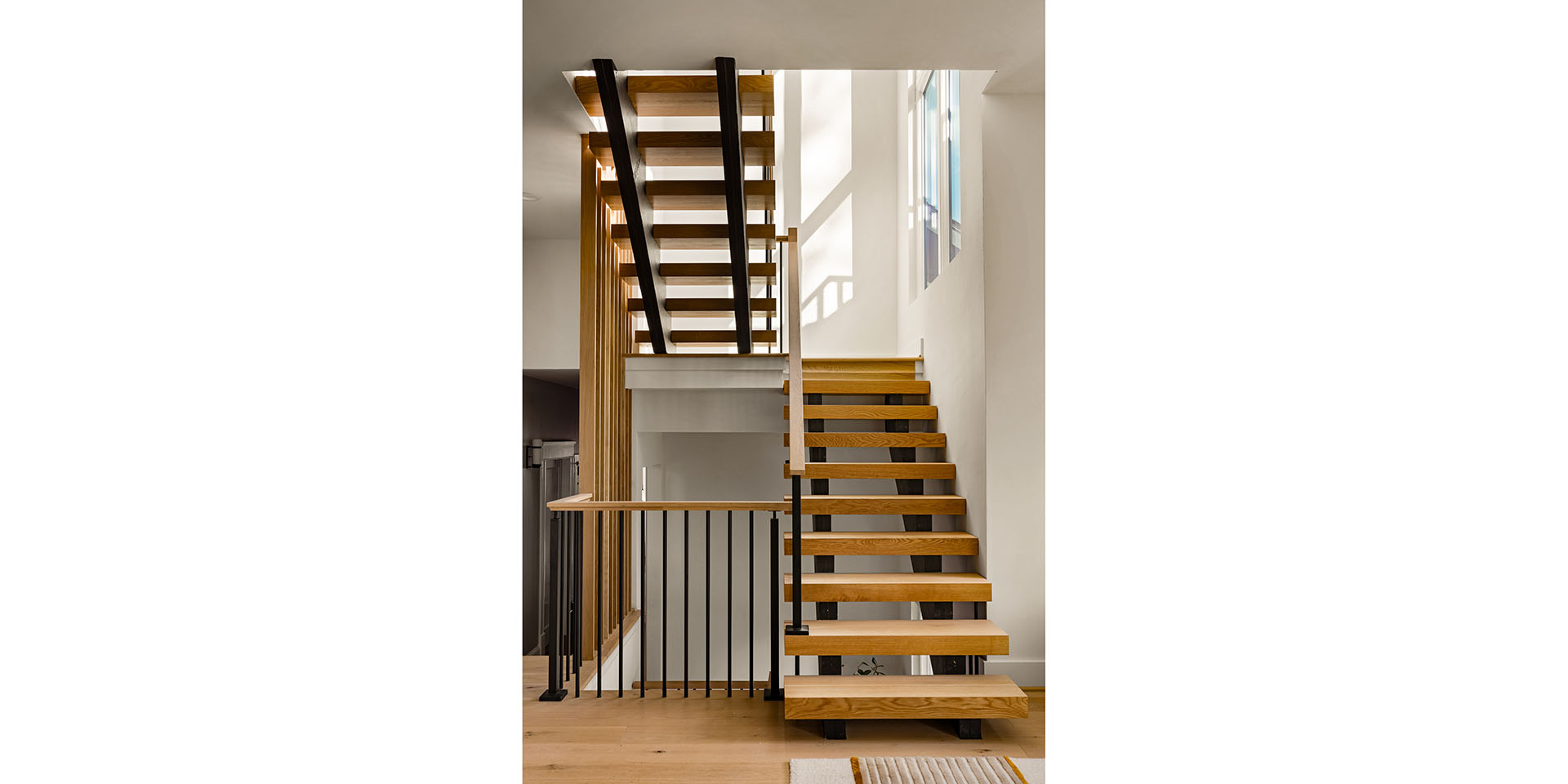 Modern wooden staircase with black metal stringers in a bright, minimalist interior.