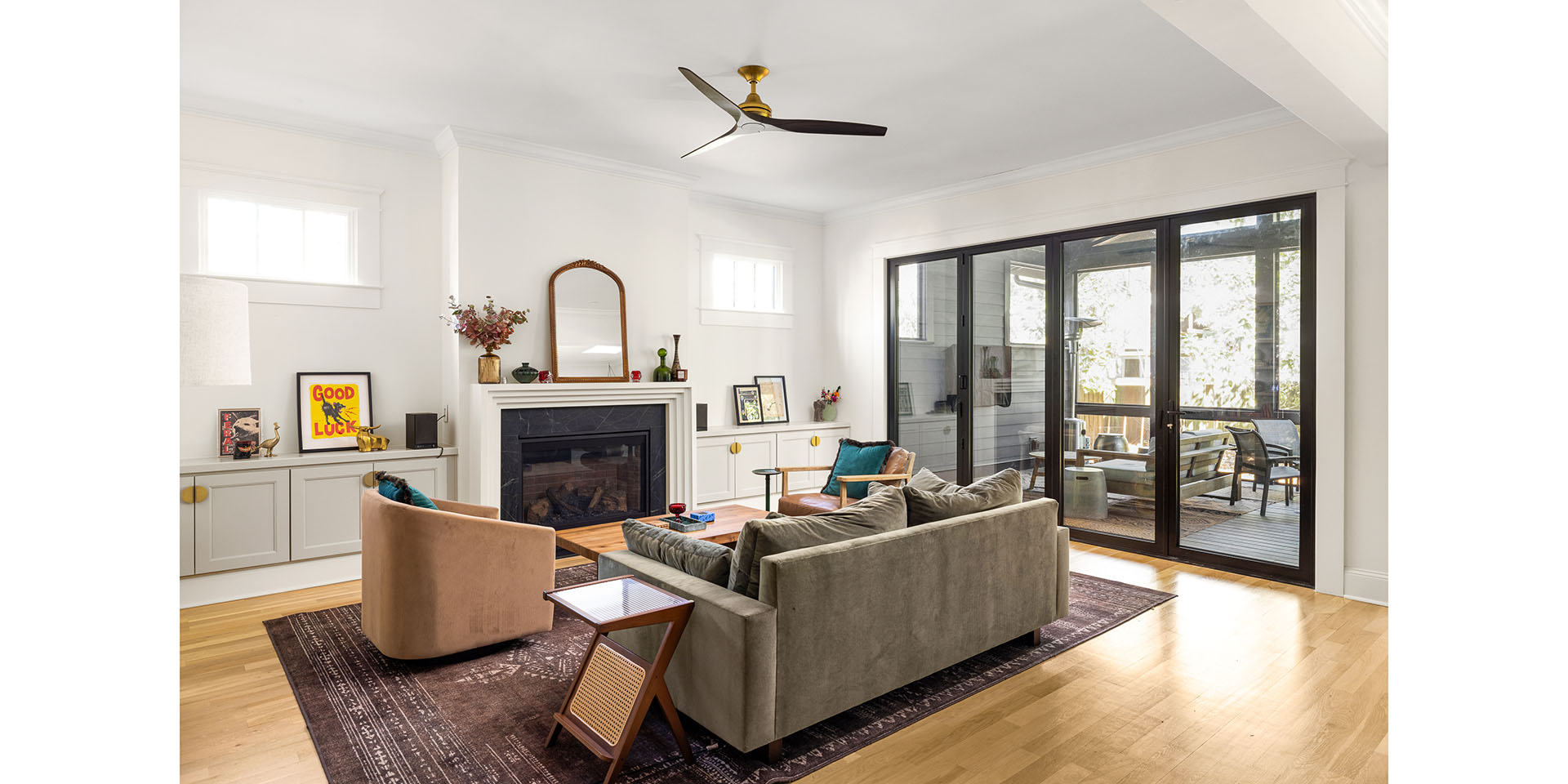 Bright living room with white walls, fireplace, built-in cabinets, and a large sliding glass door to a patio deck outside