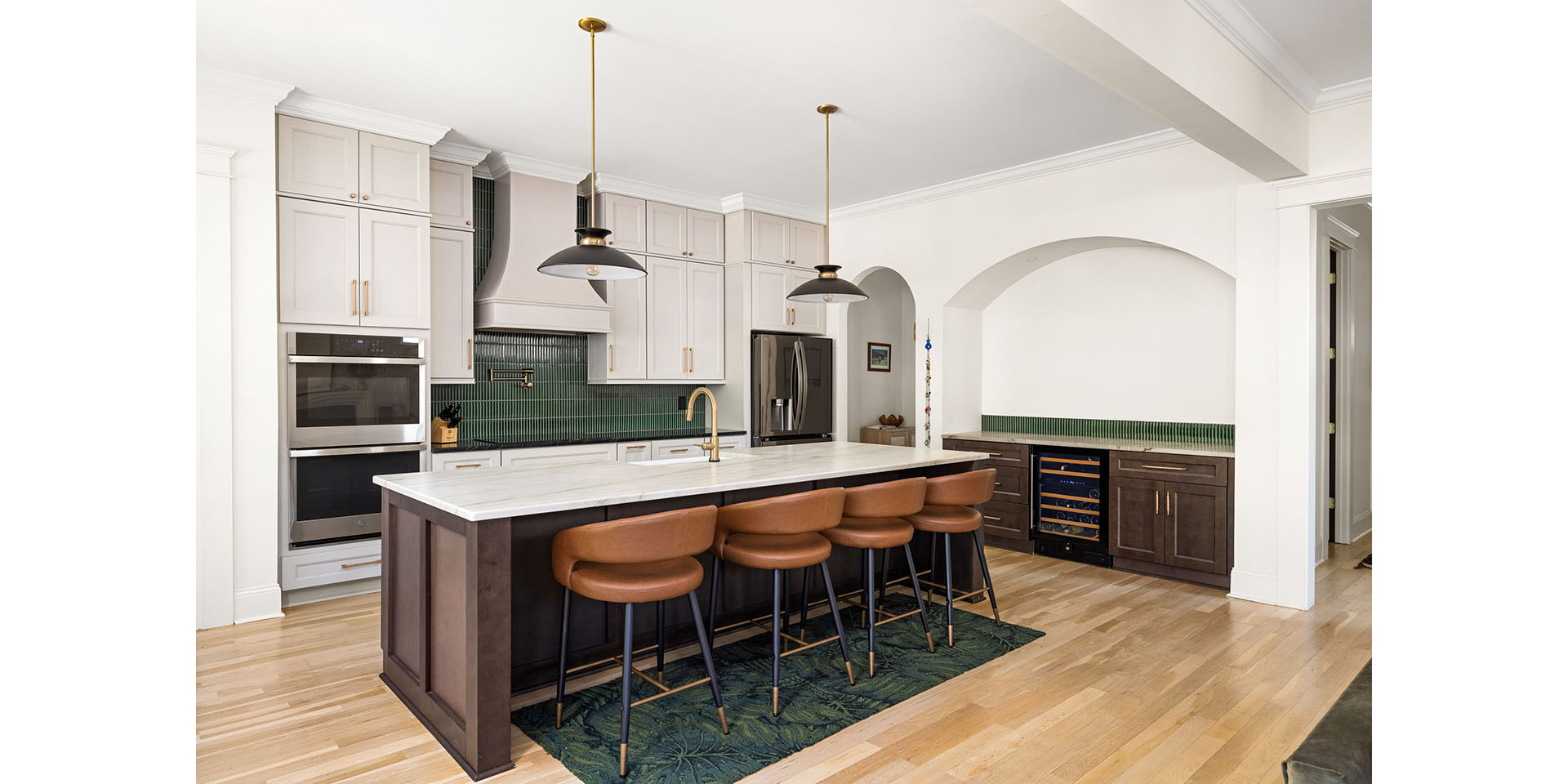 Modern kitchen with white cabinetry, green subway tile backsplash, and a dark wood island with brown leather stools.